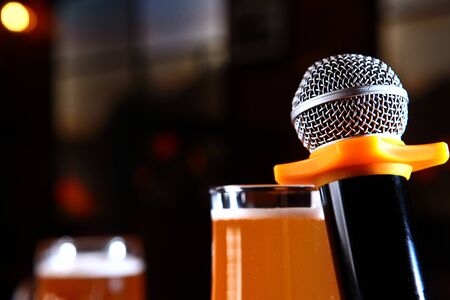 Microphone and a glass of beer on a dark background in the interior. The concept of a karaoke restaurant. Copy space.の写真素材