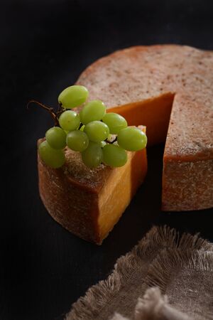 A triangular piece of hard cheese with grapes. A piece of cheese is cut off from a whole head of cheese. Copy space.Top view.の写真素材