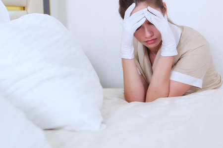 The young maid covered her face with her hands.Unrecognizable photo. The concept of cleaning. Headache. Copy space. Photo in the interior.の写真素材