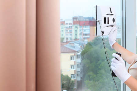 The maid installs a robot window cleaner on the glass. Clear window. Photos in the interior. The concept of cleaning and cleanliness. Copy o space. Unrecognizable photoの写真素材