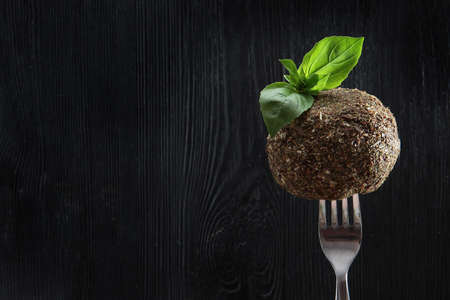 Soft dessert cheese with French herbs on a fork. Photo on a black background. Mint leaves on top....