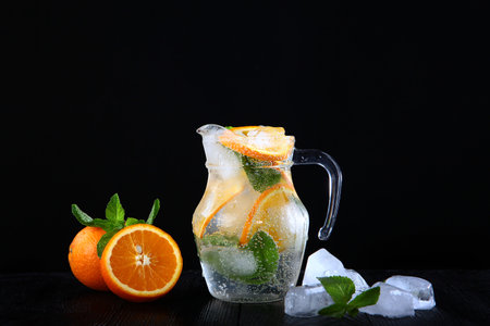 Cool lemonade made from oranges and mint in a glass jug. Ice cubes in the drink. Photo on a black background. Copy of the space.の写真素材