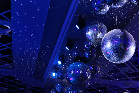 Several sparkling disco balls rotate with flashing lights during a music group performance or dance party. The party lights up disco balls on a blue background. Disco ball with bright rays.の写真素材