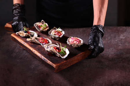 Two types of oysters with savory sauces on a wooden Board. Stylish serving dishes. Oyster season. Unrecognizable photo. Close up. Top view.の写真素材