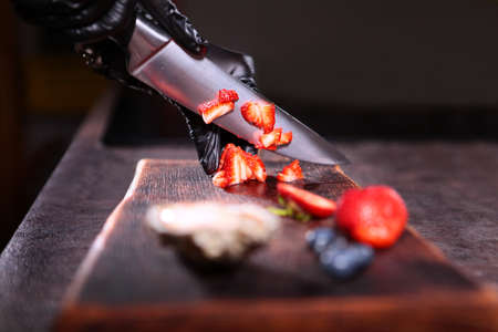 Strawberries are cut into small pieces. Preparation of berry sauce for oysters. Unrecognizable...