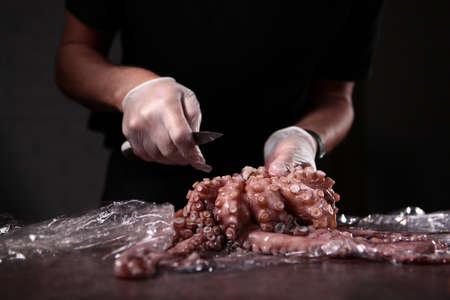 The process of cutting the carcass of boiled octopus. The removal of the eye. Knife in the hands of the chef.Unrecognizable photo. Copy space.の写真素材