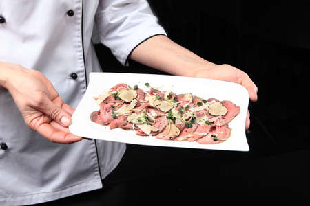 Roast beef with black truffles. The finished dish is in the hands of the chef. Unrecognizable person. Photo on a black background. Top view. Copy space.の写真素材