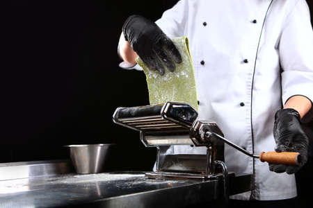 The chef prepares pasta with spinach. Close up. Unrecognizable person.Machine for preparing pasta or a pasta machine. Copy space. Black background.Vertical photo.の写真素材