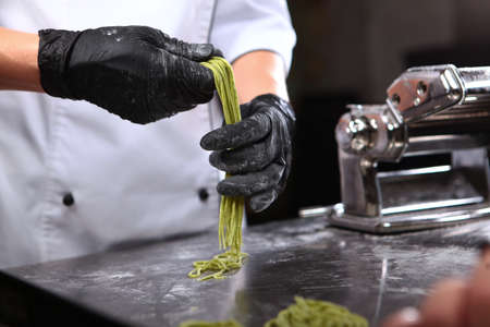 The chef holds a freshly prepared spaghetti with spinach in his hand. Useful natural ingredient. The pasta is homemade. Hands in protective gloves.の写真素材
