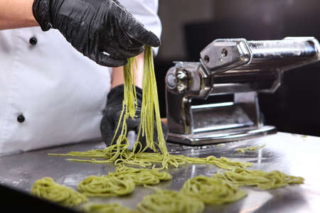 The cook is holding spaghetti with spinach. Machine for cooking pasta. Natural ingredient. The concept of home cooking. Unrecognizable person. Close up. Photo on a black background.の写真素材