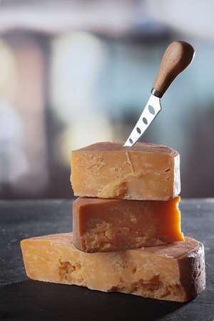 Long-aged cheese chunks. Hard cheese with a knife on a dark background. Top view. Firm texture of...