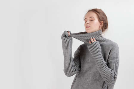 A young girl in a gray wool sweater. Sweater with a long collar. Photo on a light background. oncept of warm clothing. With copy space. Natural wool. Clothes for the cold season.の写真素材