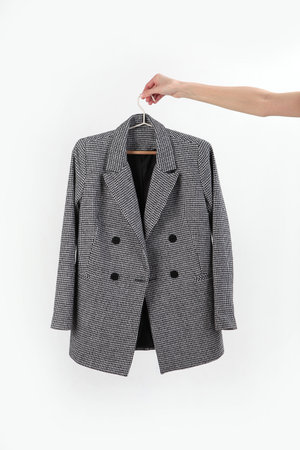 Jacket in a classic gray check on a hanger. A hand holds a jacket on a hanger. Vertical photo....