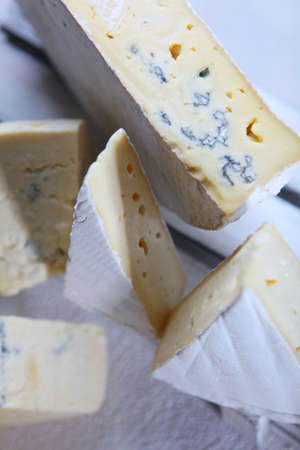 Soft white cheese with blue mold in a white wooden box on a white plate. Vertical photo. Several pieces of cheese. Assorted cheese. Out of focus. Top view.の写真素材