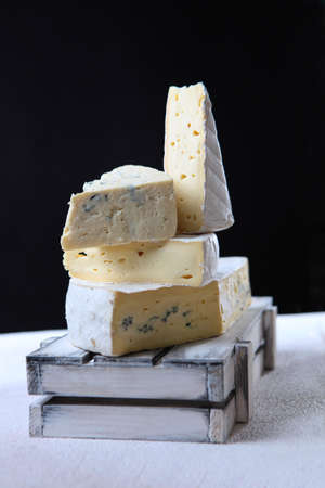 Soft white cheese with blue mold in a white wooden box on a black background. Vertical photo....
