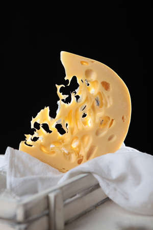 A large piece of hard maasdam cheese on a black background. Cheese with lots of holes. Dutch...