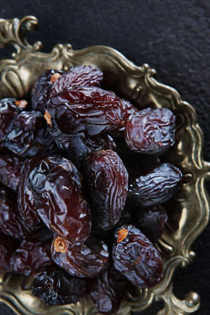 Ripe dates on an old copper platter. Juicy dried fruits. Healthy food. Fast food. Food for vegetarians. Vertical photo. Top view.の写真素材