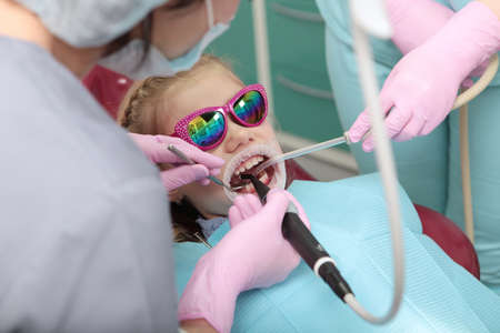 A little girl is being examined by a dentist. Examination and professional dental hygiene. Prevention of dental caries. A child wearing safety glasses. Photo inside the clinic.の写真素材