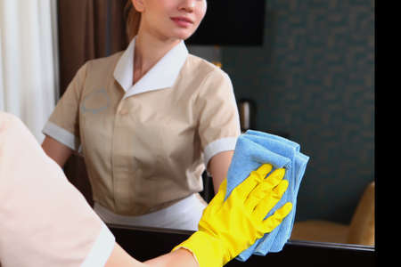 The maid wipes the mirror. Reflection in the mirror. Hands in protective gloves. Cleaning and disinfection of the hotel. The concept of the hotel business. Unrecognizable person.の写真素材