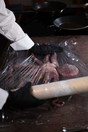 The cook wraps the whole octopus in plastic wrap. Food wrapper. Seafood dishes. Protein food. Vertical photo without people.の写真素材