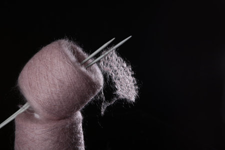 The concept of hobby knitting. The yarn is fluffy pink with knitting needles on a black background. Free space. Knitting on knitting needles. Natural wool mohairの写真素材