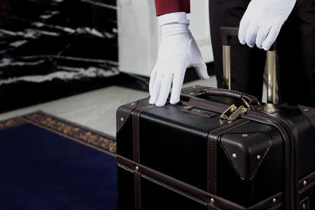 The doorman is holding a suitcase. Unrecognizable photo. Only white-gloved hands. Hotel service....
