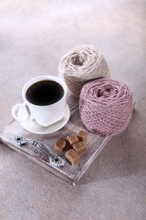 A cup of coffee on a tray and two skeins of natural wool for knitting next to it. A hobby or...