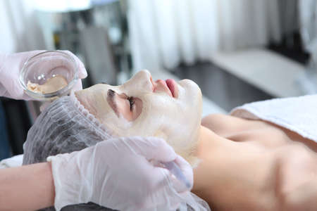 The face of a young woman close-up on the procedure in a cosmetology clinic. Applying the mask to the face. The concept of youth and facial skin care.の写真素材