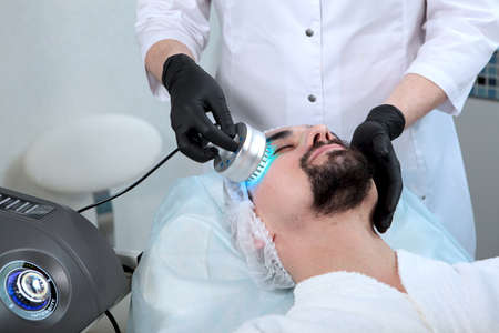 A man doing facial treatments in a cosmetic clinic. Mens cosmetology. Hardware cosmetology. The...