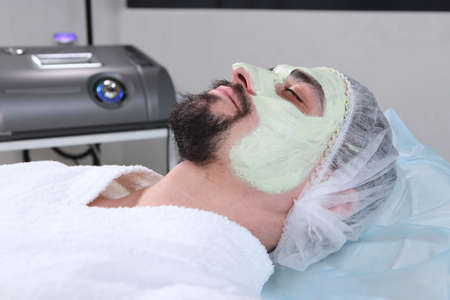 Cosmetic mask on a mans face. Man doing facial procedures in a cosmetic clinic. Mens cosmetology. The concept of preservation of youth and skin care of face.の写真素材