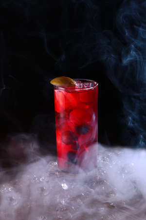 Homemade lemonade made from berries in a tall glass. Vertical photo on a black background. Chunks of ice. Smoke on a black background.の写真素材