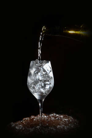 White wine is poured into a glass with ice. Vertical photo on a black background. Chunks of ice. Refreshing drink.の写真素材