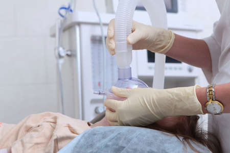 Doctor holds an oxygen mask on child's face. Work of doctor and an assistant resuscitation specialist before the operation. Health care and life saving concept. Vertical photo.Unrecognizable people.の写真素材