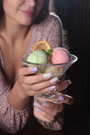 Girl holds ice cream in her hands. Multicolored ice cream balls. Ice cream in a glass bowl. Unrecognizable person.Vertical photo on a dark background.Out of focus.の写真素材