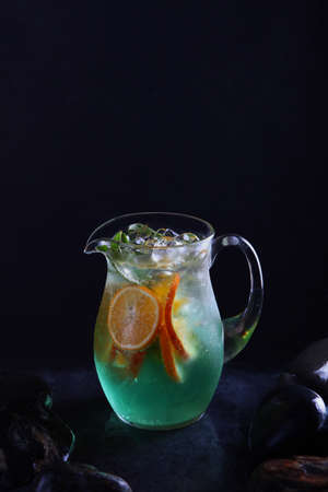 Classic non-alcoholic Mojito lemonade. Homemade cold lemonade. Fresh fruits in a glass jug. Black background. Vertical photo. Copy space.の写真素材