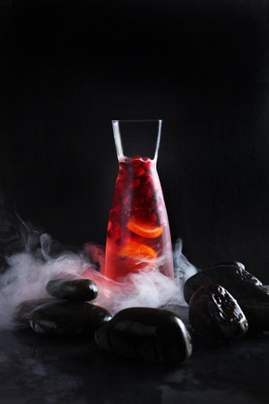 Homemade cold berry lemonade. Fresh berries in a misted glass jug. Pieces of ice. Black background. Vertical photo. Refreshing drink. Quench thirst.の写真素材