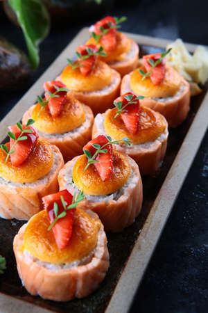 Baked Philadelphia rolls with strawberries and salmon. Traditional Japanese food. Vertical photo on black background. White ginger. Close-up. Out of focus.の写真素材