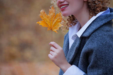 Young girl walking in the park in autumn. Girl smiles and holds an autumn maple leaf in her hand. Unrecognizable person.の写真素材