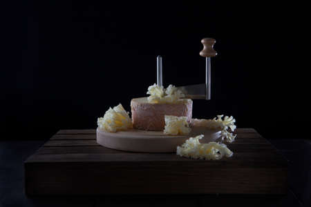 The tete de moine cheese is cut with special girolle knife. A type of Swiss semi-hard cheese made from unpasteurized cow's milk called a monk's head.Cheese on a wooden round board.の写真素材