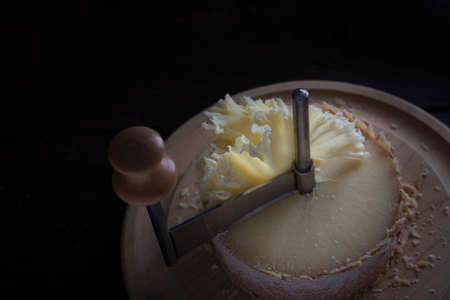 A Swiss semi-hard cheese made from unpasteurized cow's milk called a monk's head. The cheese stands on a wooden round board. Special girolle knife.With copy space.の写真素材