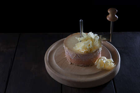 A Swiss semi-hard cheese made from unpasteurized cow's milk called a monk's head. The cheese stands on a wooden round board. Special girolle knife.With copy space. Vertical photo on black background.の写真素材