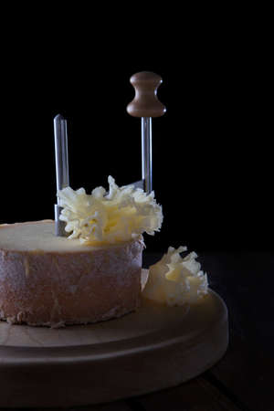 Cheese tete de moine on a wooden round board. Close-up of cheese texture. Side view. Vertical photo on a black background.の写真素材