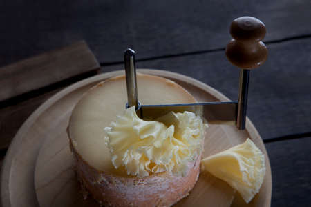 Special girolle knife. Thin shavings of tete de moine cheese. Cheese on a wooden round board. Close-up of cheese texture.の写真素材