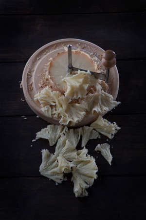Swiss cheese tete de moine sliced into shavings on a round wooden surface. A scraper or girolle knife for slicing and tasting delicious cheese shavings. Vertical photo.の写真素材