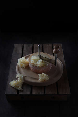 The tete de moine cheese is cut into thin shavings. Special girolle knife for slicing this cheese. Cheese on wooden round board stands on a wooden box. Sliced cheese slices.Copy spaceの写真素材