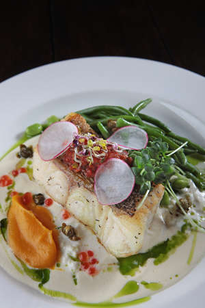 Pike perch with white sauce and beans. A white plate. Menu for the restaurant. Healthy and low-calorie food. A dish of fish with beans.Close-up.の写真素材