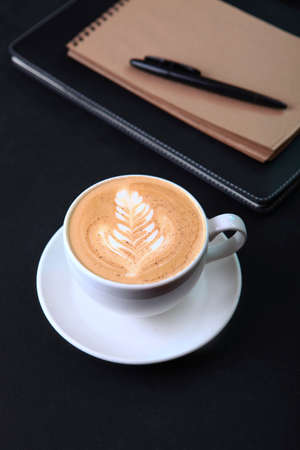 A cup of coffee on a black background. A notepad for writing and a ballpoint pen. The concept of a business breakfast or coffee break. Food and drinks. Top view. Space for copying. Flat lay.の写真素材