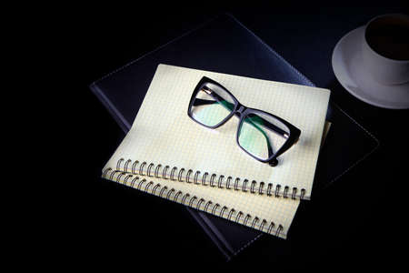 A notebook for notes and eyeglasses are on the table. Black background. The concept of a business breakfast or coffee break. Food and drinks.の写真素材