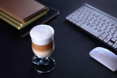Coffee drink in a tall glass. Coffee latte. Computer keyboard and notebooks for writing on a black background.The concept of a business breakfast or coffee break. Food and drinks.の写真素材