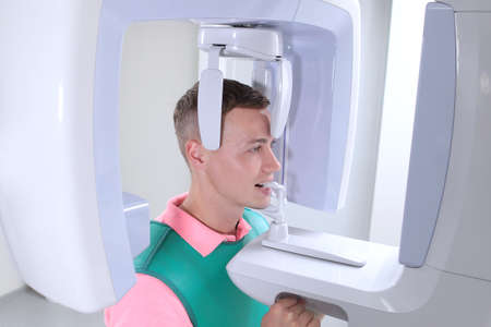 X-ray room in a modern dental clinic. Modern dentistry. A patient in a dental clinic takes a panoramic picture of the teeth. Prevention of dental diseases. Accurate diagnosis.Handsome man.の写真素材